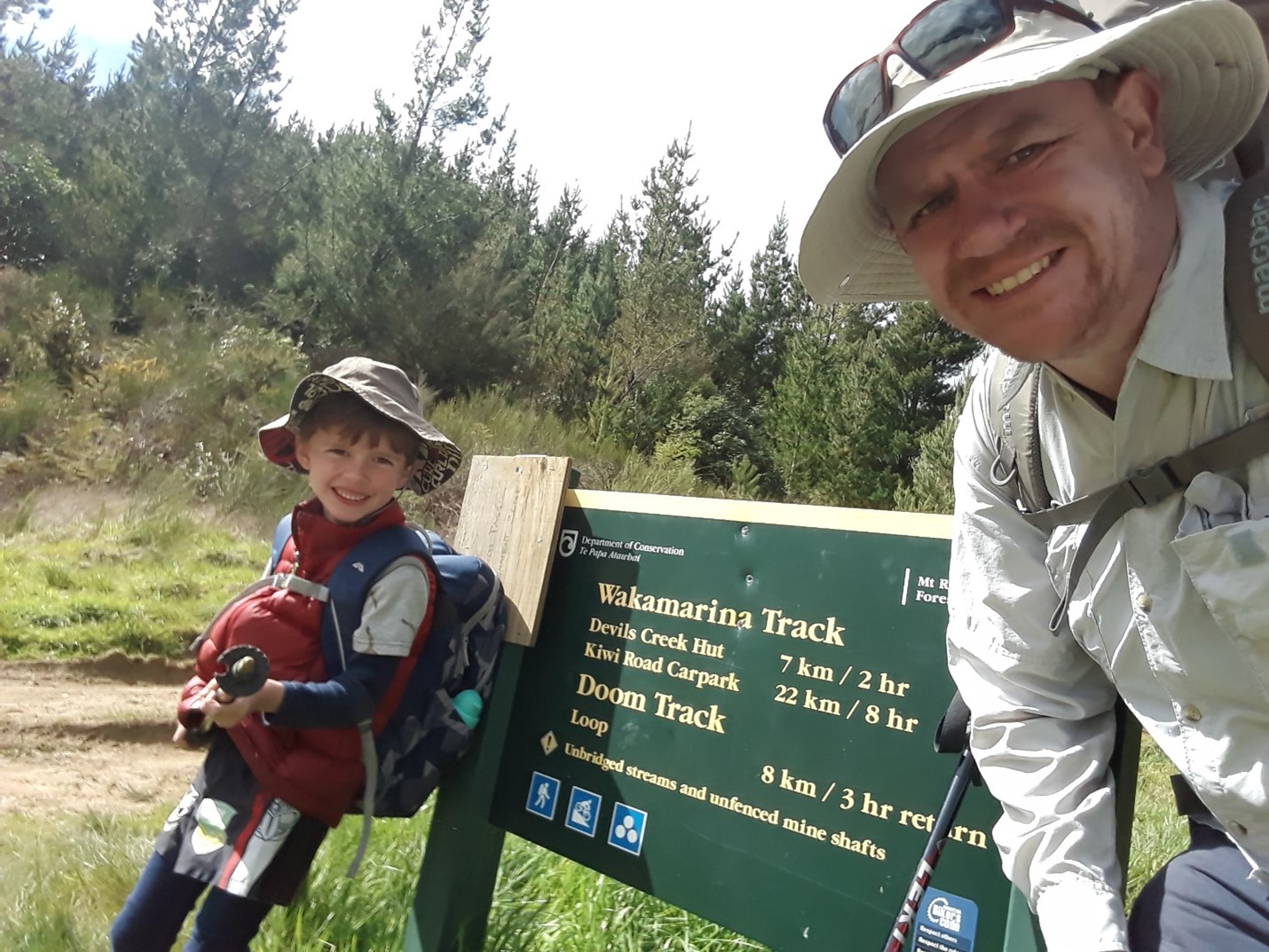 Matt Miller and son posing in front of the Wakamarina and Doom Tracks sign at a trailhead