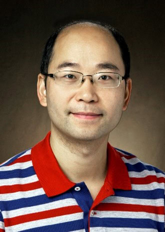 Portrait of Chen against a neutral background. He is wearing a red, white, and blue striped polo shirt, glasses, and is smiling kindly.
