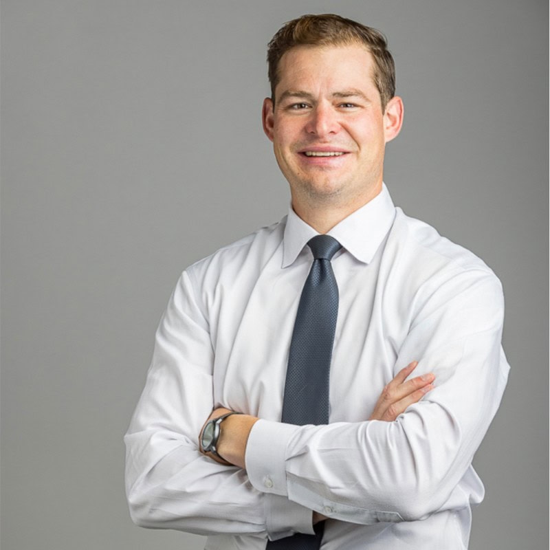 Devin Mogler, President and CEO of the National Oilseed Processors Association (NOPA), in a white shirt and blue tie, standing with arms crossed.