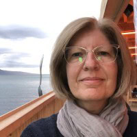 Fabiola Dionisi, Senior Advisor for Lipid Sciences at Nestlé Research, wearing glasses and a scarf, photographed outdoors with a scenic ocean view.
