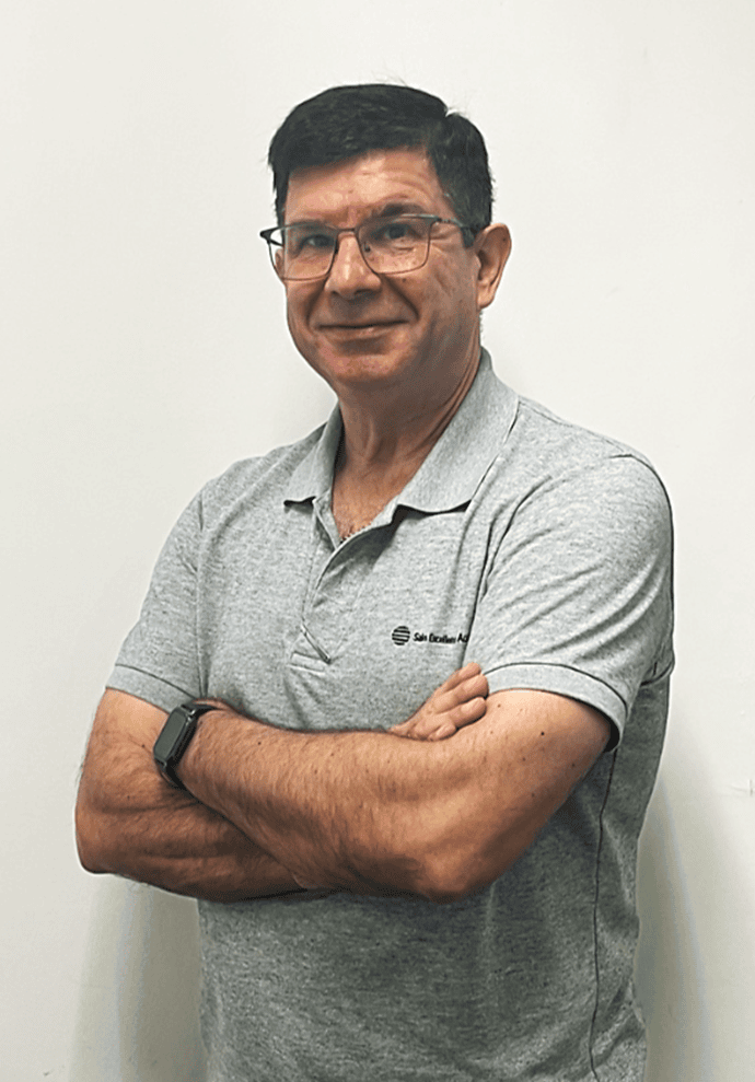 Professional portrait of an individual wearing glasses and a gray polo shirt, standing with arms crossed against a neutral background.