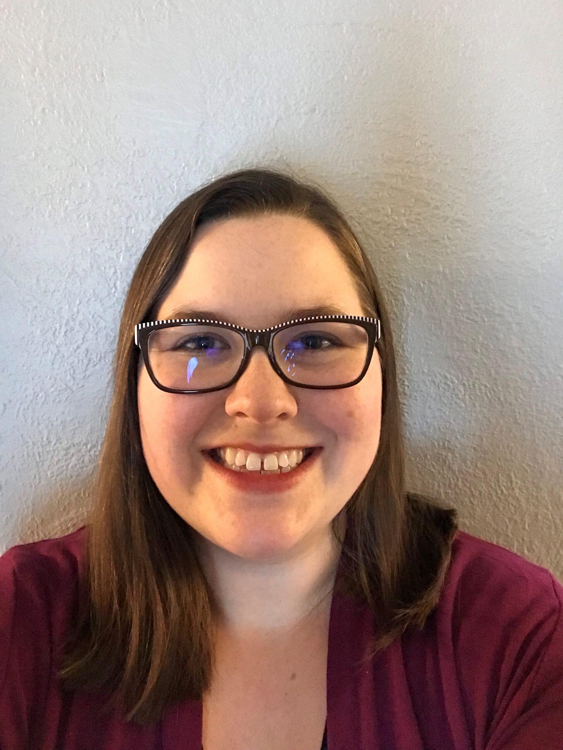 Professional portrait of a person wearing glasses and a burgundy blazer against a neutral background.