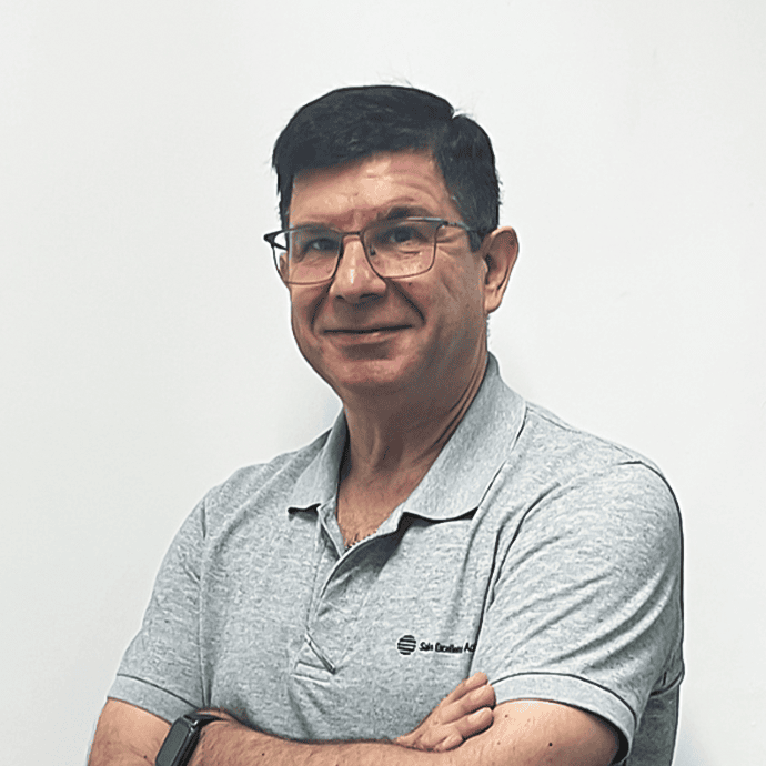 Professional headshot of a person wearing glasses and a light gray polo shirt, standing with arms crossed against a white background.