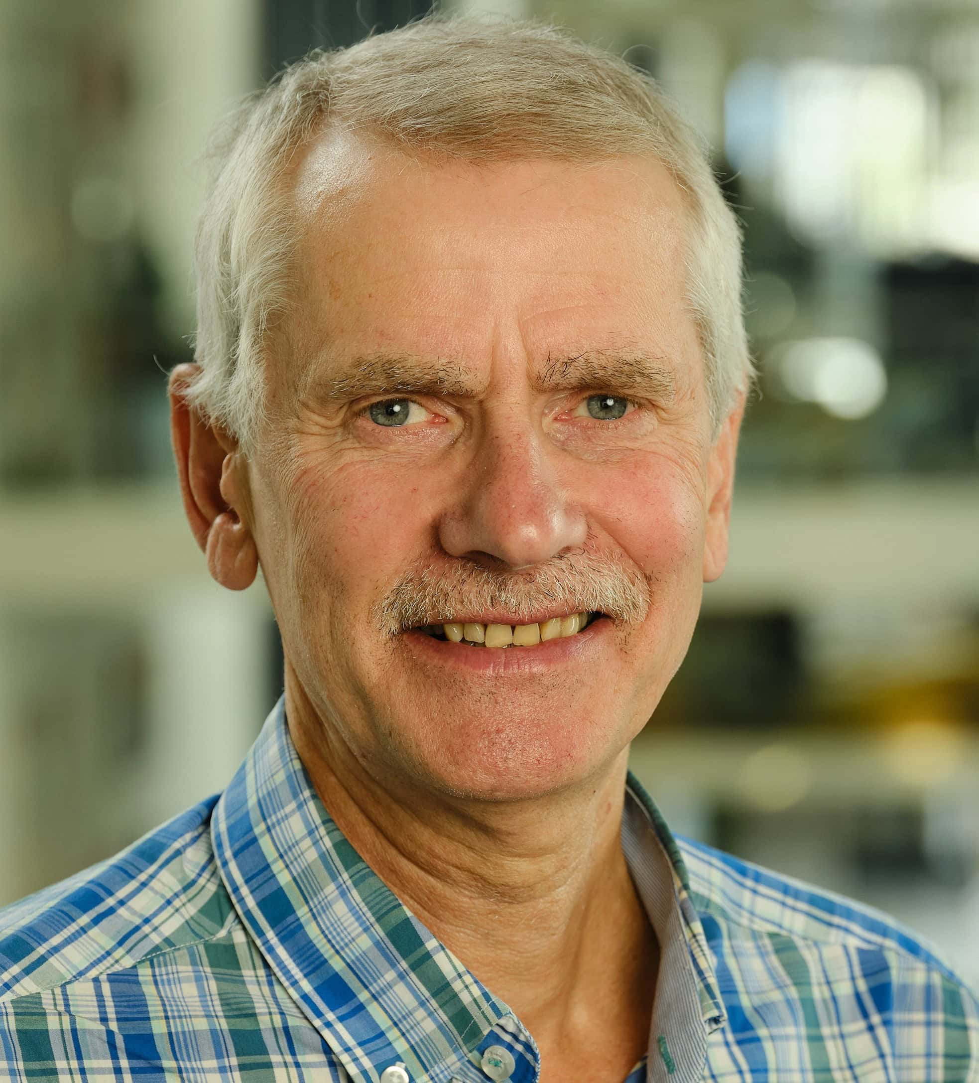 Head-and-shoulders portrait of Julian Barnes wearing a blue plaid shirt, photographed indoors with a softly blurred background.
